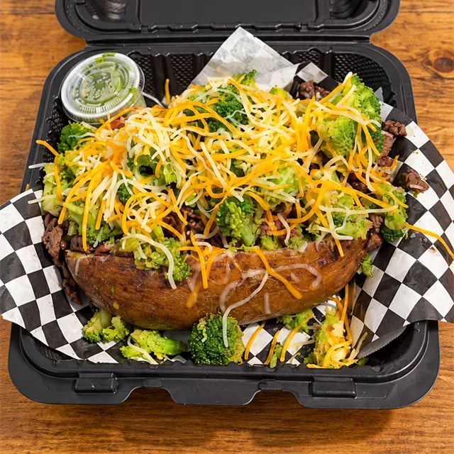 The OverFlo loaded potato piled with steak, broccoli and shredded cheese in a takeout box