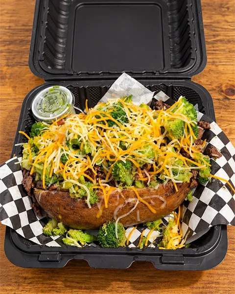The OverFlo loaded potato piled with steak, broccoli and shredded cheddar in a takeout box